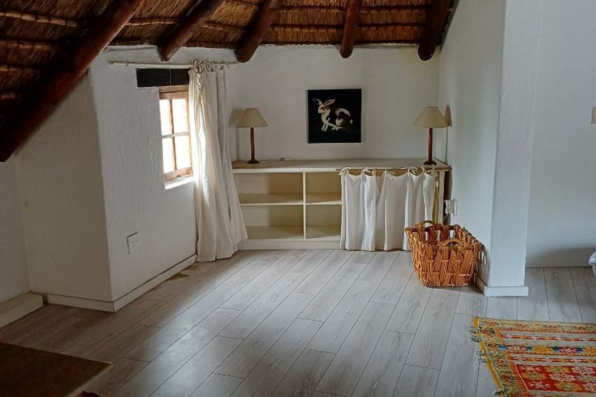 A bedroom featuring a vaulted thatched roof with exposed timber beams and modern wood-look laminate flooring.