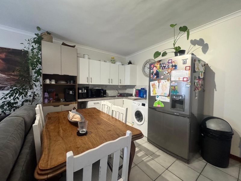 Open-plan kitchen and dining area featuring white cabinetry, tiled flooring, and integrated laundry plumbing, offering a functional layout for daily living.