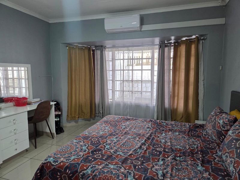 A bedroom featuring tiled flooring, a wall-mounted air conditioning unit, and a large window with security bars.
