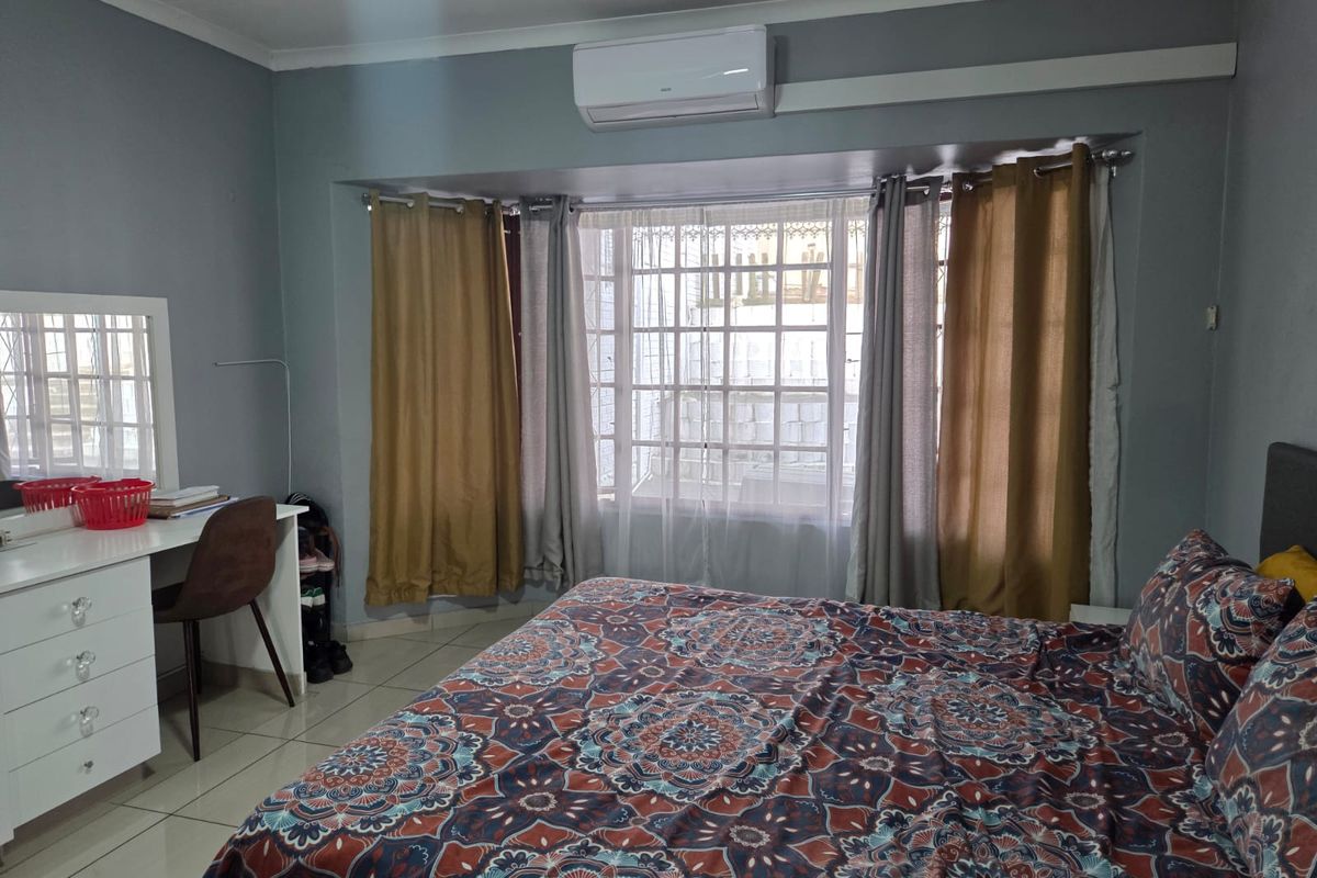 A bedroom featuring tiled flooring, a wall-mounted air conditioning unit, and a large window with security bars.