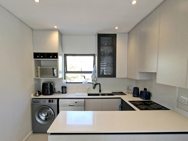 Modern kitchen featuring sleek cabinetry, quartz countertops, an electric hob, and integrated space for laundry and dishwashing appliances.