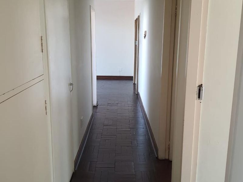 A long, empty hallway featuring dark parquet flooring and built-in storage cupboards, providing access to various rooms within the apartment.