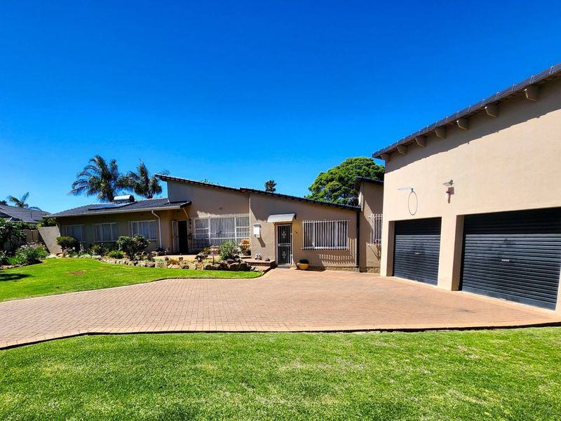 Front view of a well-maintained house featuring a paved driveway, double garage, landscaped garden, and security features on windows.