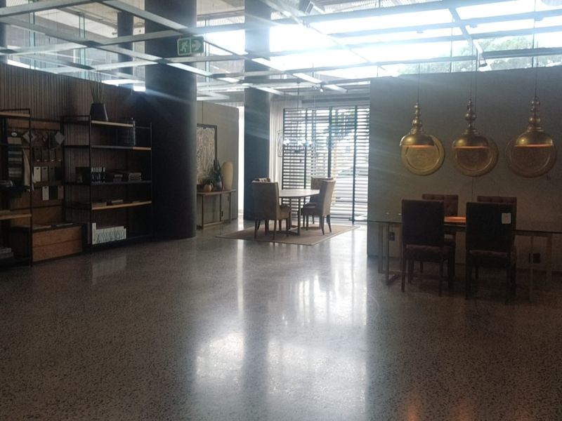 Spacious open-plan retail or showroom area featuring polished concrete floors, exposed structural columns, and a modern grid ceiling system with integrated lighting.