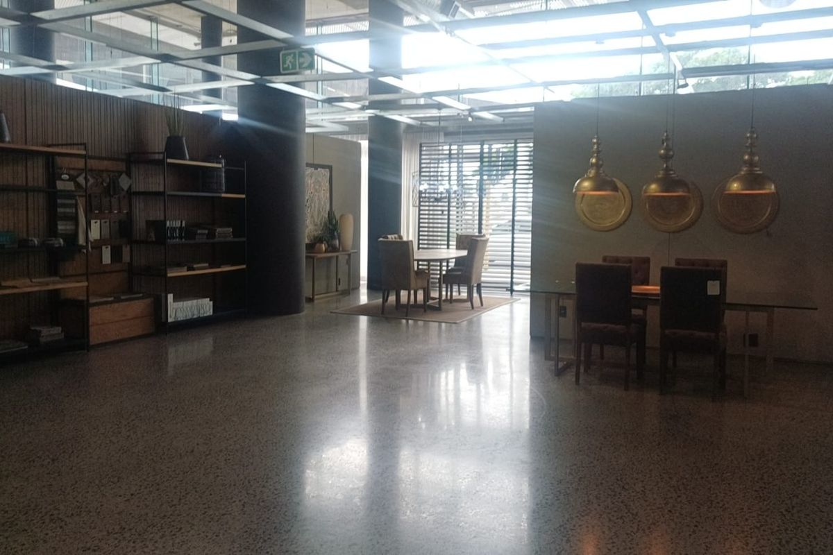 Spacious open-plan retail or showroom area featuring polished concrete floors, exposed structural columns, and a modern grid ceiling system with integrated lighting.