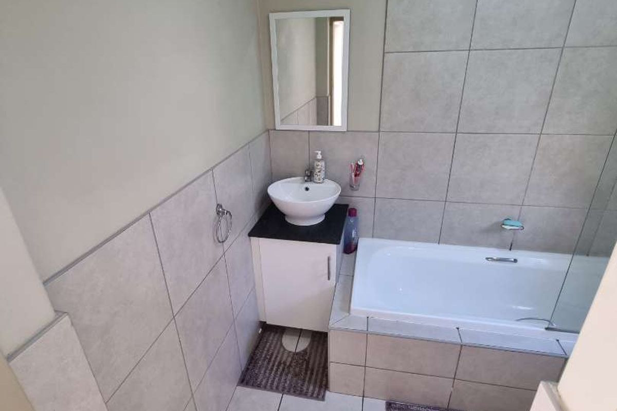 A functional bathroom featuring a built-in bathtub, a vanity with a vessel sink, and neutral wall and floor tiling.