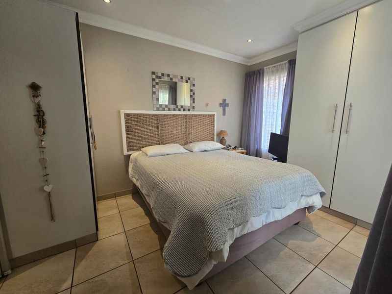 A well-maintained bedroom featuring neutral tiled flooring, built-in cupboards, and recessed downlighting, offering a clean and functional living space.