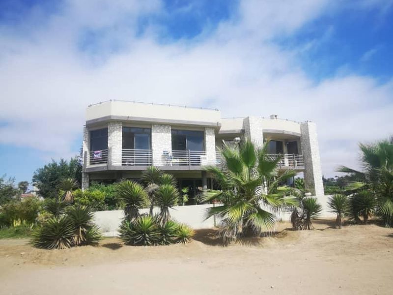 A two-story residential property featuring stone cladding, balcony access, and large glass windows, set within a landscaped garden area.
