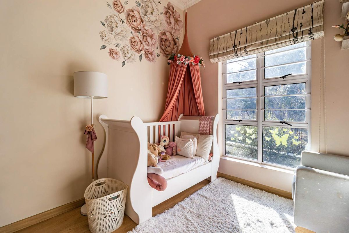 A well-maintained bedroom featuring laminate flooring, large aluminium-framed windows with a roman blind, and soft neutral wall tones.