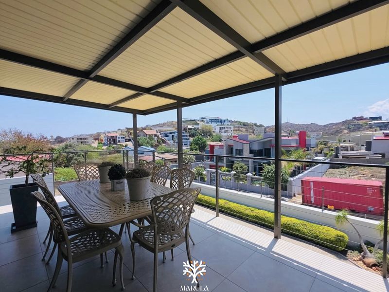 Spacious covered balcony featuring modern tiled flooring, a sleek glass balustrade, and panoramic views of the surrounding neighborhood.