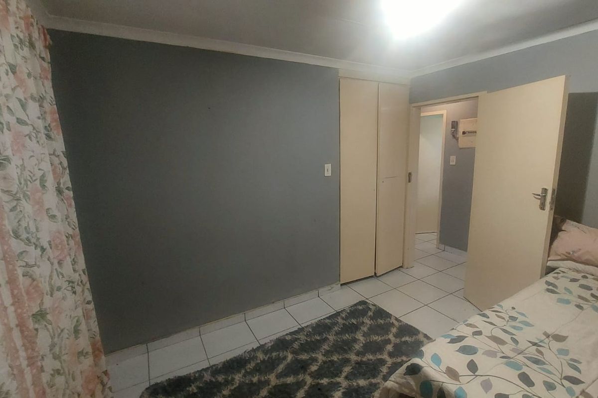 A bedroom featuring tiled flooring, built-in cupboards, and neutral grey wall finishes, providing a functional and simple living space.