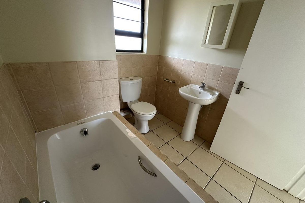 A functional bathroom featuring a standard bathtub, pedestal basin, and toilet with neutral wall and floor tiling.