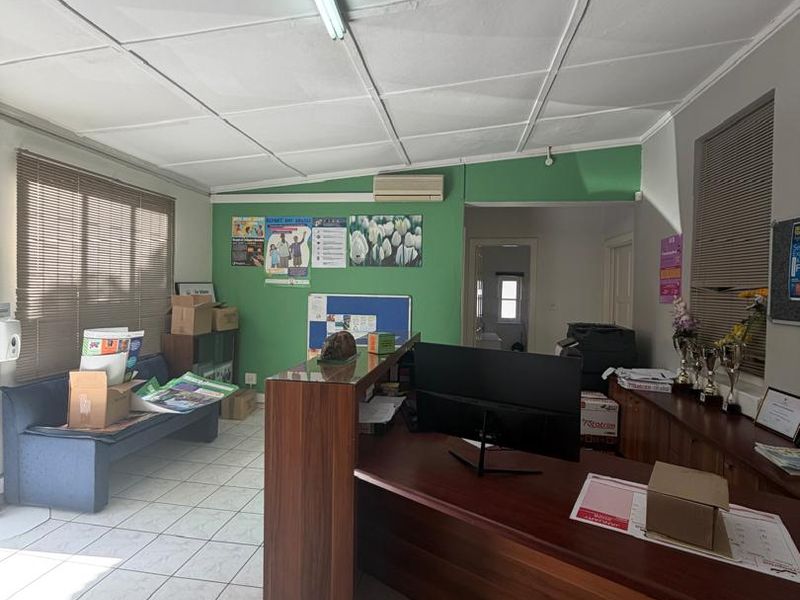 A functional office space featuring tiled flooring, a drop ceiling with integrated lighting, and a wall-mounted air conditioning unit.