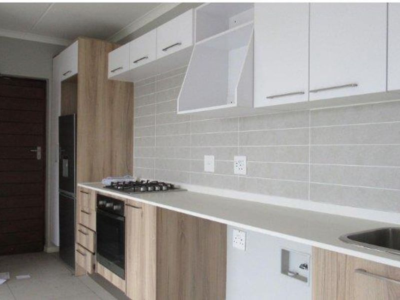 Modern kitchen featuring light wood-tone and white cabinetry, gas hob, built-in oven, tiled backsplash, and integrated plumbing for appliances.