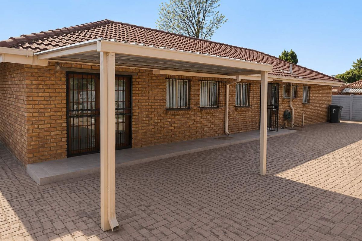 Rear exterior view of the house featuring a brick facade, tiled roof, and a covered patio area with paved surroundings.
