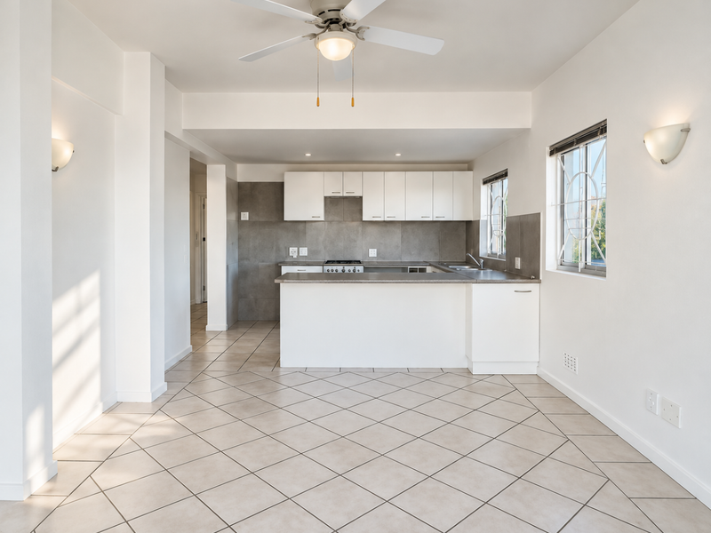 Spacious open-plan kitchen and living area featuring neutral tiled flooring, modern cabinetry, built-in gas hob, and ample natural light from large windows.
