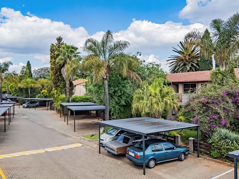 An elevated view of an apartment complex parking area featuring multiple covered carports, paved driveways, and established garden landscaping.