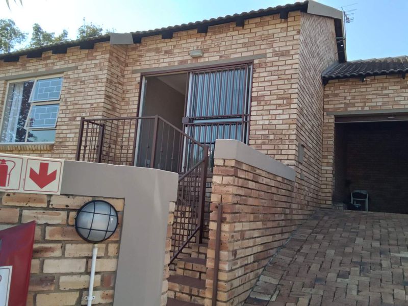 Front exterior view of a face brick townhouse featuring a paved driveway, integrated garage, and a raised entrance with security gate.