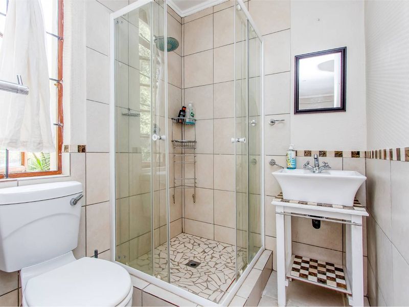 A functional bathroom featuring a glass-enclosed shower, vessel sink with vanity stand, and neutral ceramic tiling throughout.