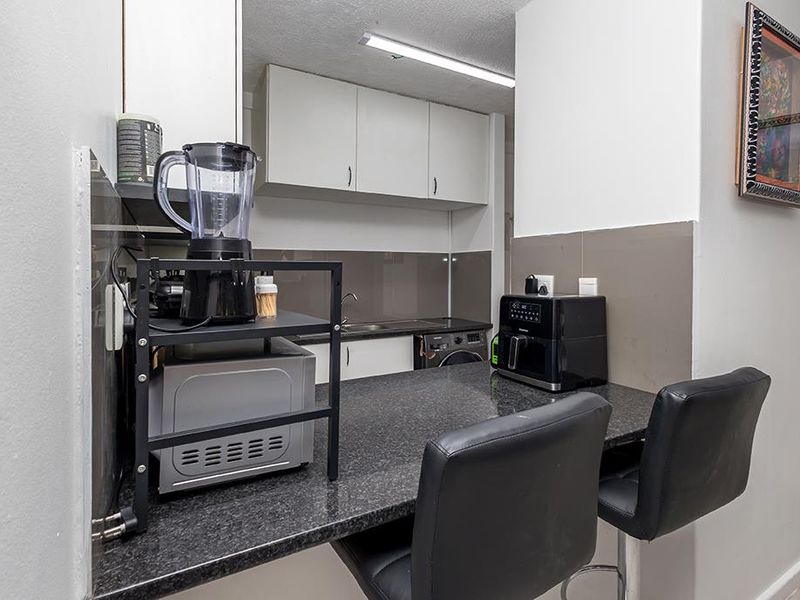 Compact kitchen featuring granite countertops, built-in cabinetry, a stainless steel sink, and an integrated washing machine.