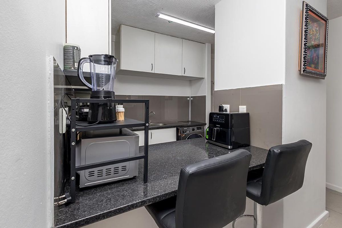 Compact kitchen featuring granite countertops, built-in cabinetry, a stainless steel sink, and an integrated washing machine.