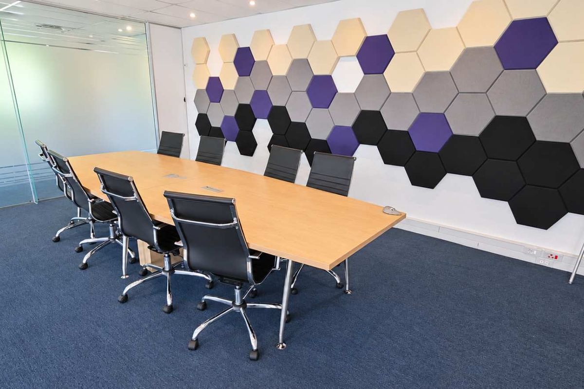 Modern office meeting room featuring glass partitions, acoustic hexagonal wall panels, recessed lighting, and professional carpet flooring.
