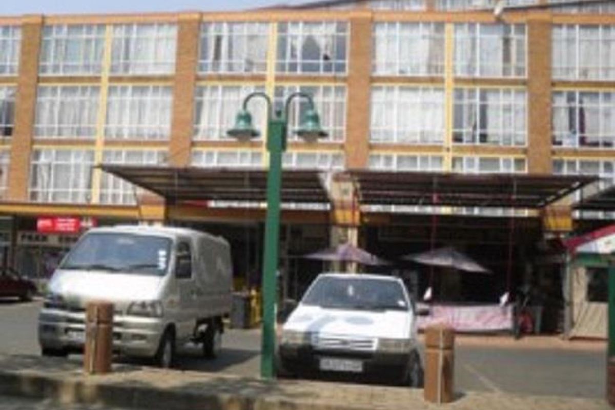Front elevation of a multi-story commercial building featuring a brick facade, large glass windows, and a covered ground-level walkway with parking space.