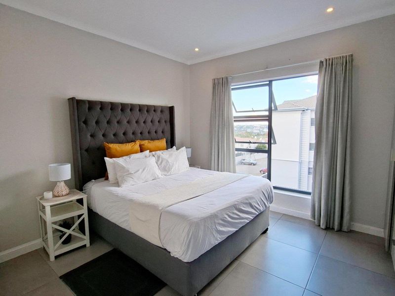 A well-maintained bedroom featuring neutral wall tones, large format floor tiles, recessed lighting, and built-in storage with a view through the window.