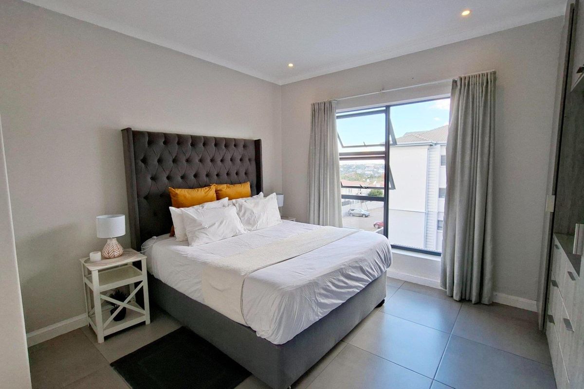 A well-maintained bedroom featuring neutral wall tones, large format floor tiles, recessed lighting, and built-in storage with a view through the window.