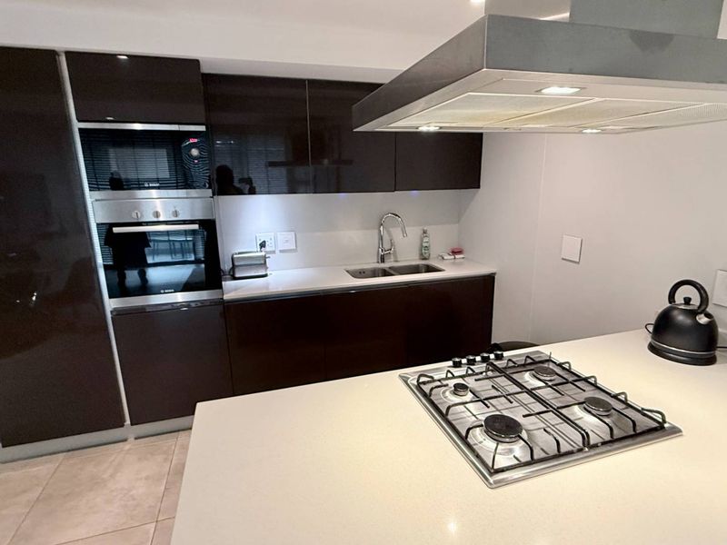 Modern kitchen featuring high-gloss cabinetry, stone countertops, a central island with a gas hob, built-in oven, and a stainless steel extractor fan.