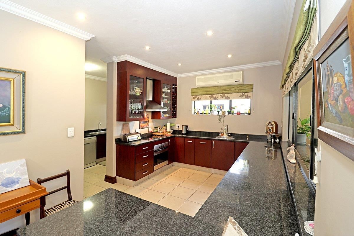 A well-maintained kitchen featuring dark wood cabinetry, granite countertops, integrated appliances, and a breakfast bar, with an adjacent scullery area.