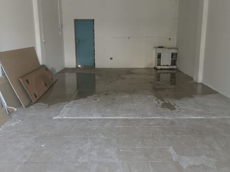 An empty, open-plan commercial space featuring tiled flooring and a suspended ceiling, currently showing signs of water damage and requiring maintenance.