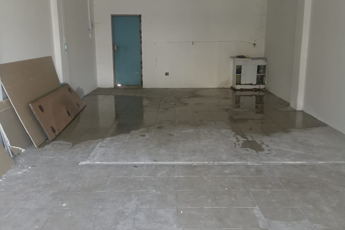 An empty, open-plan commercial space featuring tiled flooring and a suspended ceiling, currently showing signs of water damage and requiring maintenance.