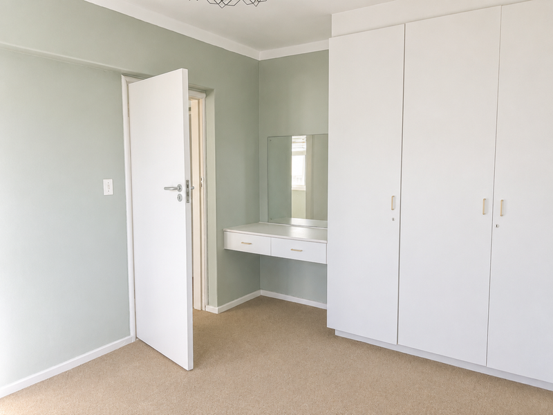 A clean, well-maintained bedroom featuring neutral wall tones, ample built-in cupboard storage, and a dedicated built-in vanity area with a mirror.