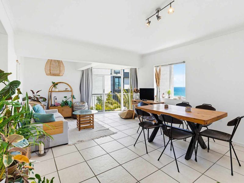 Bright open-plan living and dining area featuring tiled flooring, track lighting, and direct access to a balcony with ocean views.