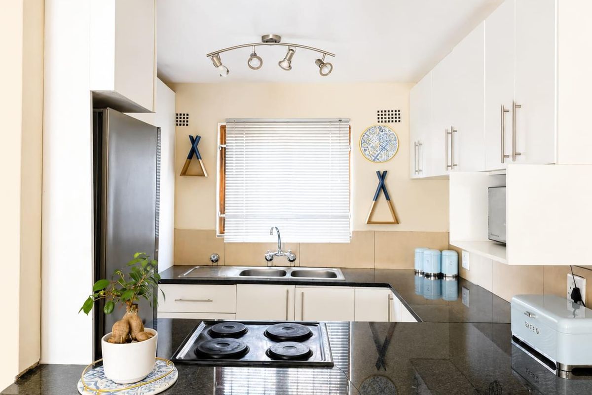 A functional kitchen featuring white cabinetry, dark granite countertops, a double basin sink, and an integrated electric hob with overhead track lighting.