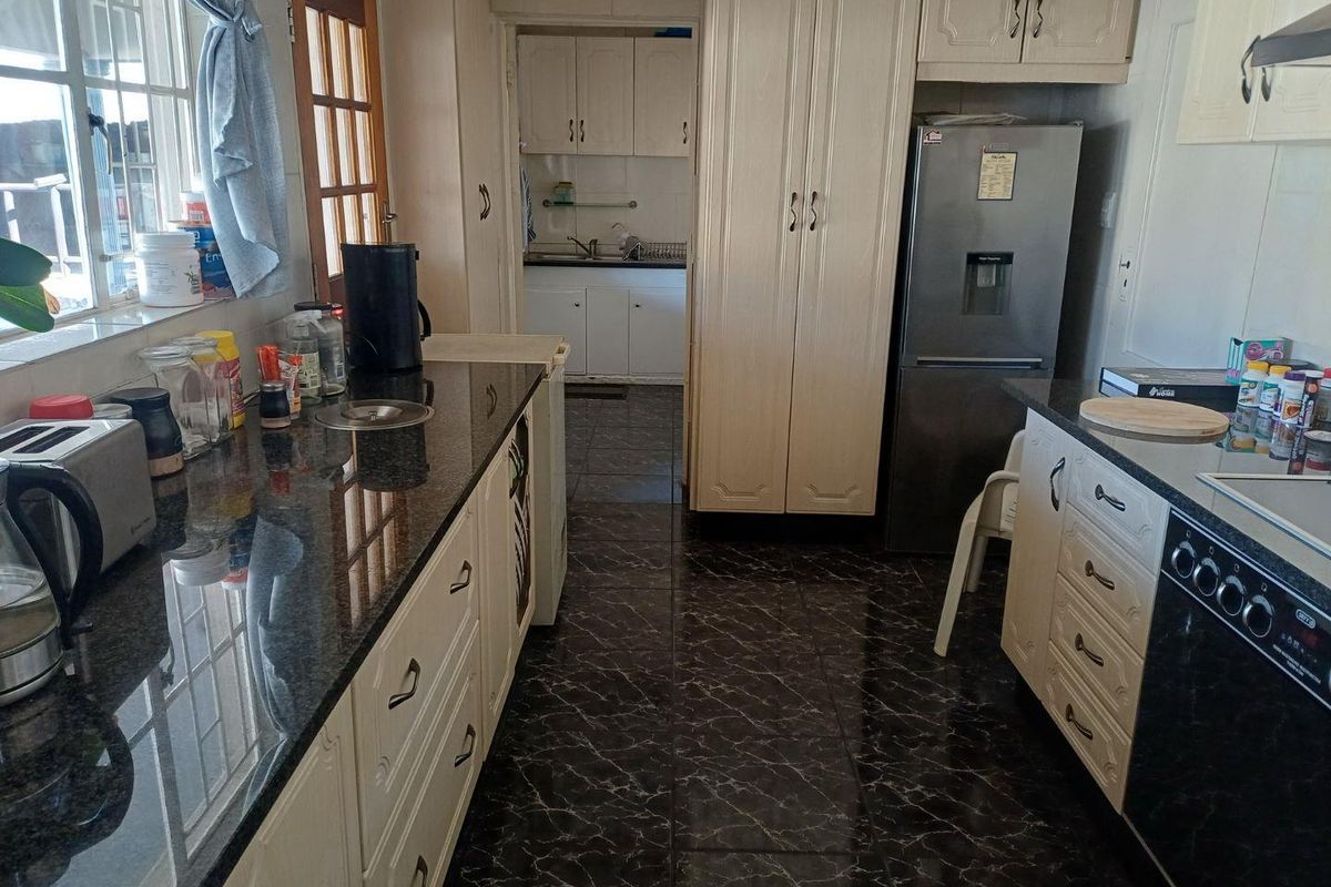 A functional kitchen featuring granite countertops, ample built-in cabinetry, and a tiled floor, with an adjacent scullery area visible in the background.