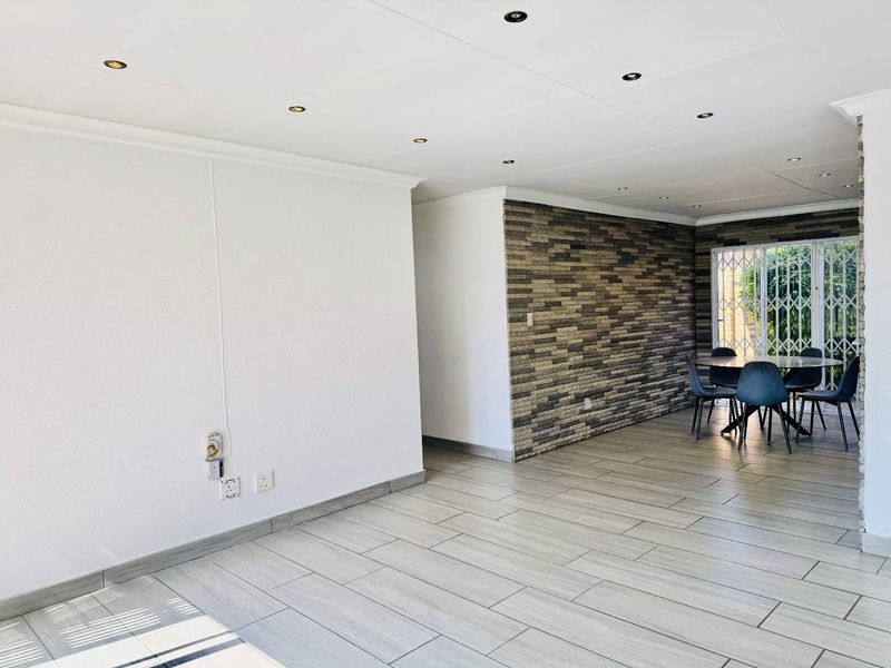 Spacious open-plan living area featuring modern tiled flooring, recessed downlighting, and a decorative stone-cladding feature wall with access to the exterior.
