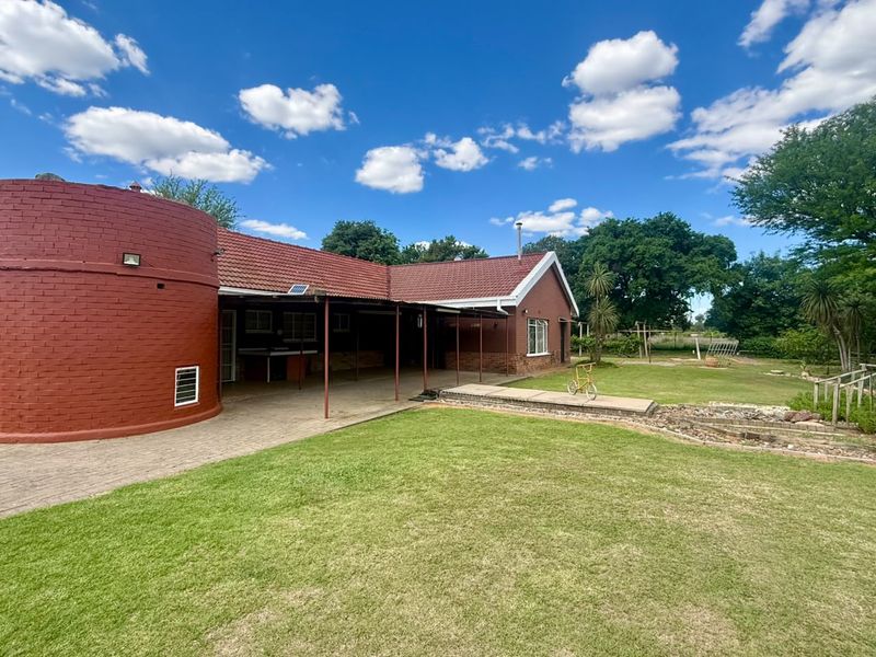 Rear view of the property featuring a red brick facade, a covered patio area, and a well-maintained lawn with paved pathways.