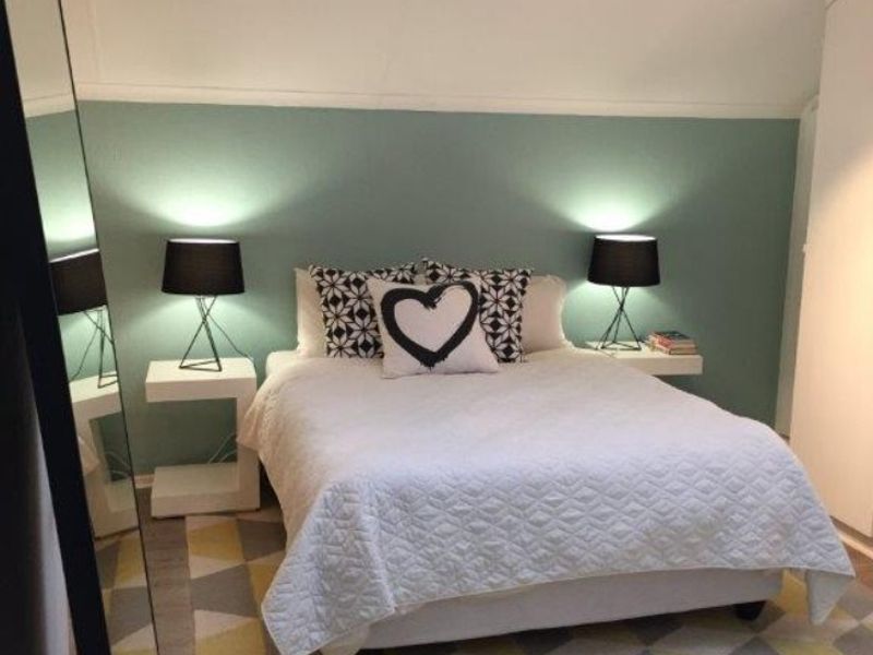 A cozy bedroom featuring a sloped ceiling, track lighting, and a built-in wardrobe, finished with a soft green accent wall.