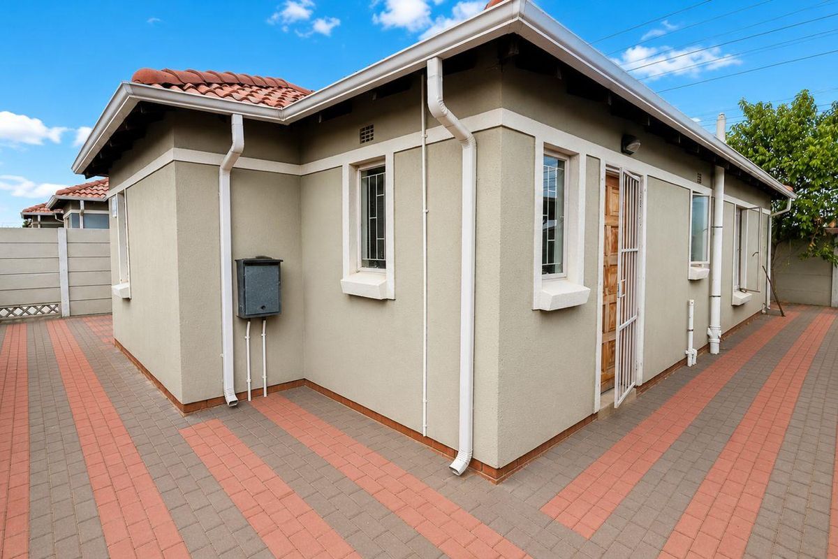 A view of the rear exterior of the house, featuring paved walkways, a tiled roof, and a secure metal security gate at the entrance.