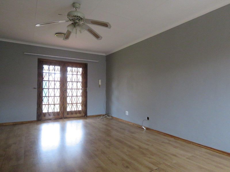An empty living room featuring laminate flooring, a ceiling fan, and wooden double doors with a security gate leading to the exterior.