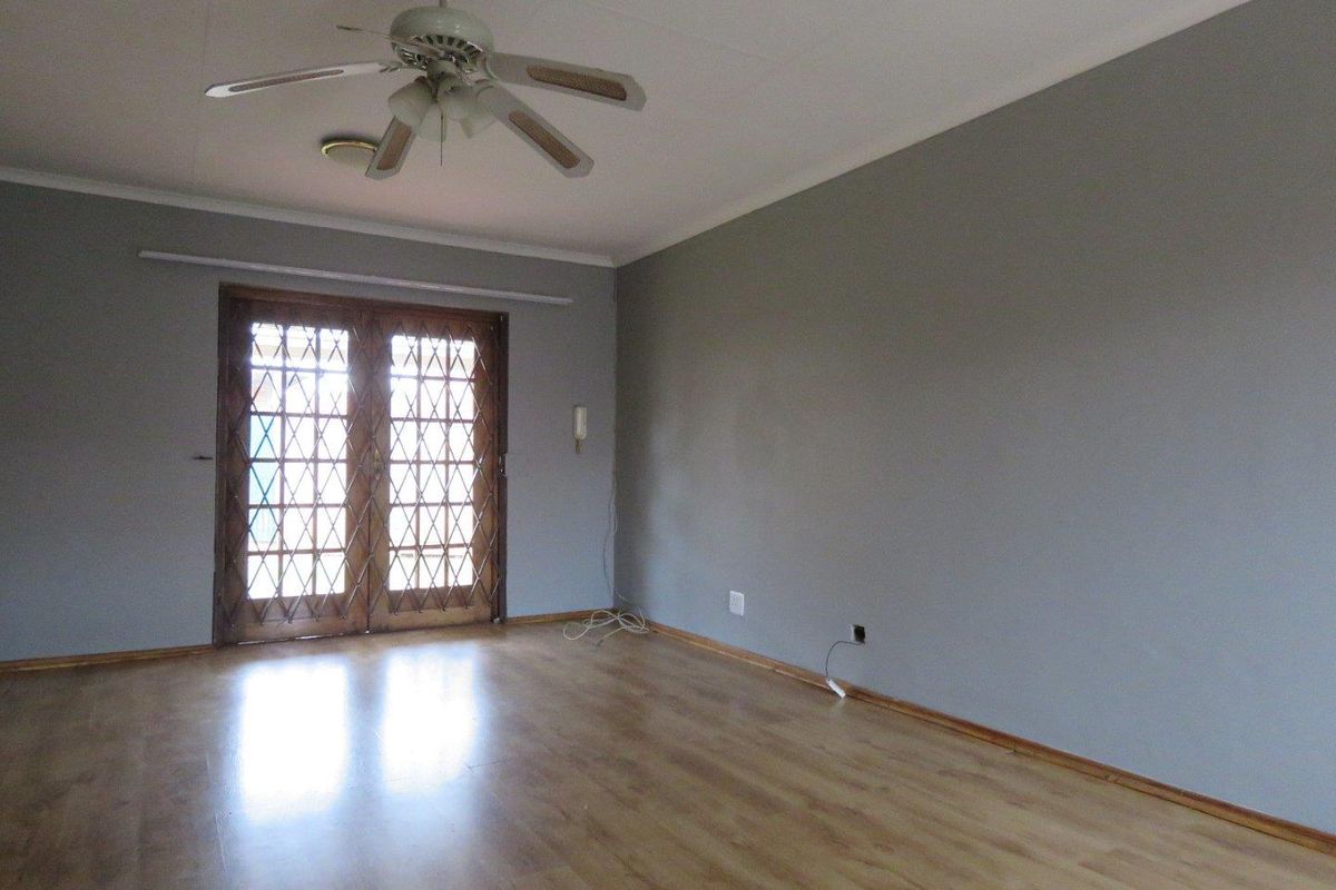 An empty living room featuring laminate flooring, a ceiling fan, and wooden double doors with a security gate leading to the exterior.