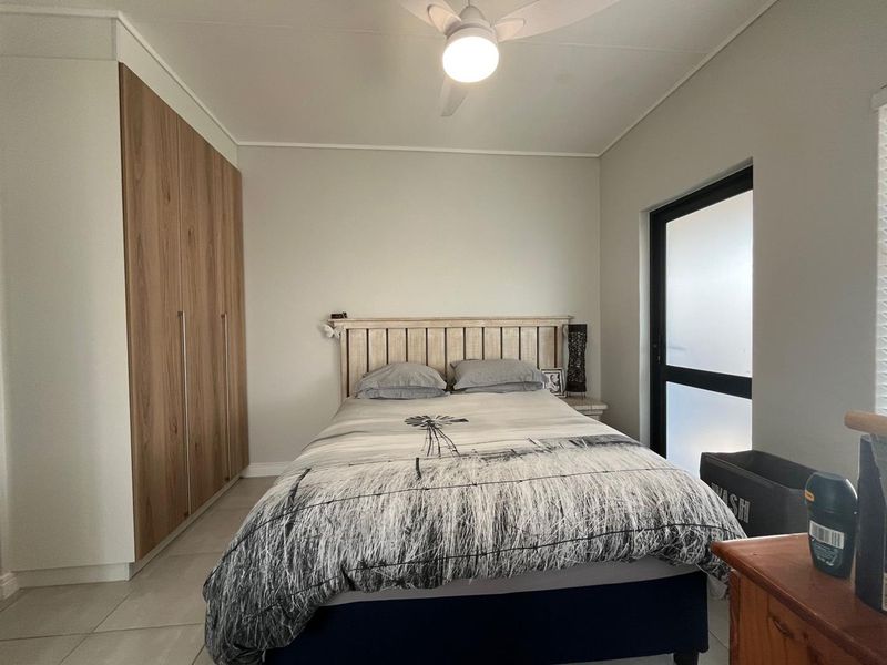 A well-maintained bedroom featuring modern wood-finish built-in cupboards, tiled flooring, and a ceiling fan with integrated lighting.