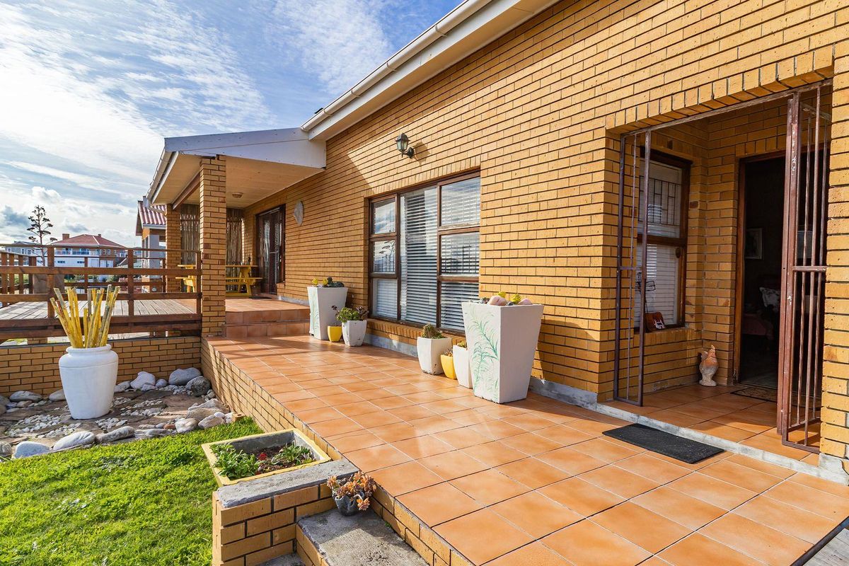 A well-maintained rear exterior featuring a brick facade, tiled patio area, and an elevated wooden deck overlooking the garden.