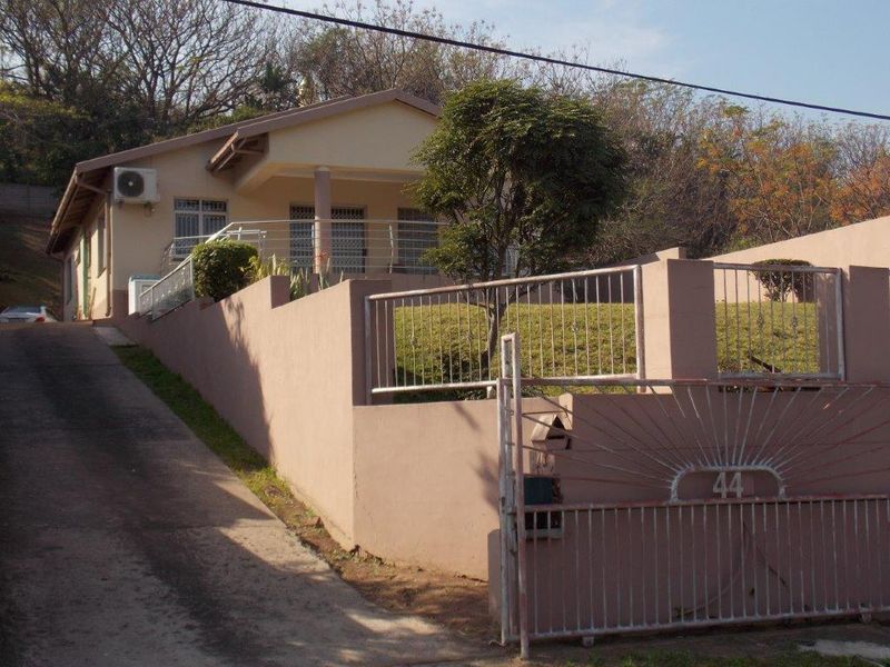 Front elevation of a single-story house featuring a concrete driveway, perimeter boundary wall with metal gate, and a covered porch entrance.
