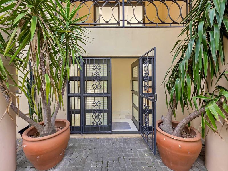 A secure entrance featuring a decorative wrought iron security gate, cobblestone paving, and a balcony above with matching iron railings.