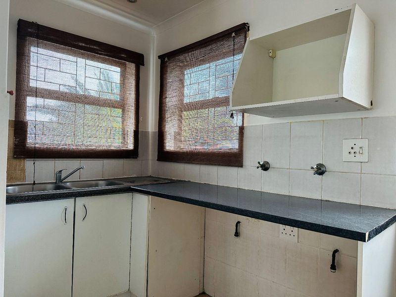 A functional kitchen space featuring laminate countertops, a stainless steel sink, tiled backsplash, and built-in cabinetry with dedicated space for appliances.