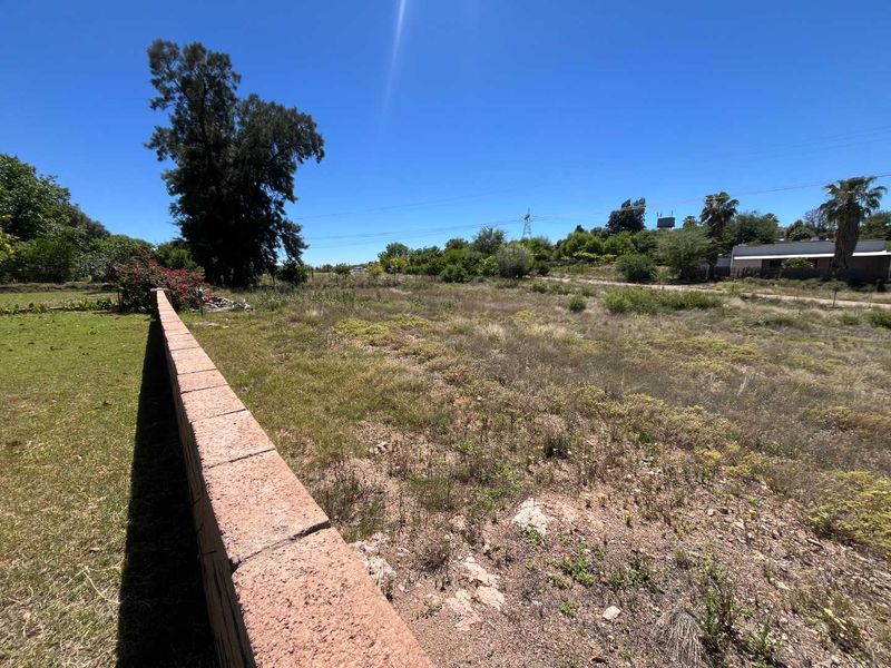 A large, undeveloped plot of land featuring a boundary wall and natural vegetation under a clear blue sky.