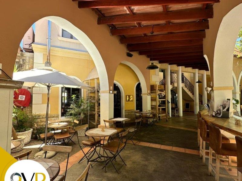 A spacious covered outdoor patio featuring exposed timber beams, arched architectural columns, and a built-in bar area, ideal for office breakout or social space.